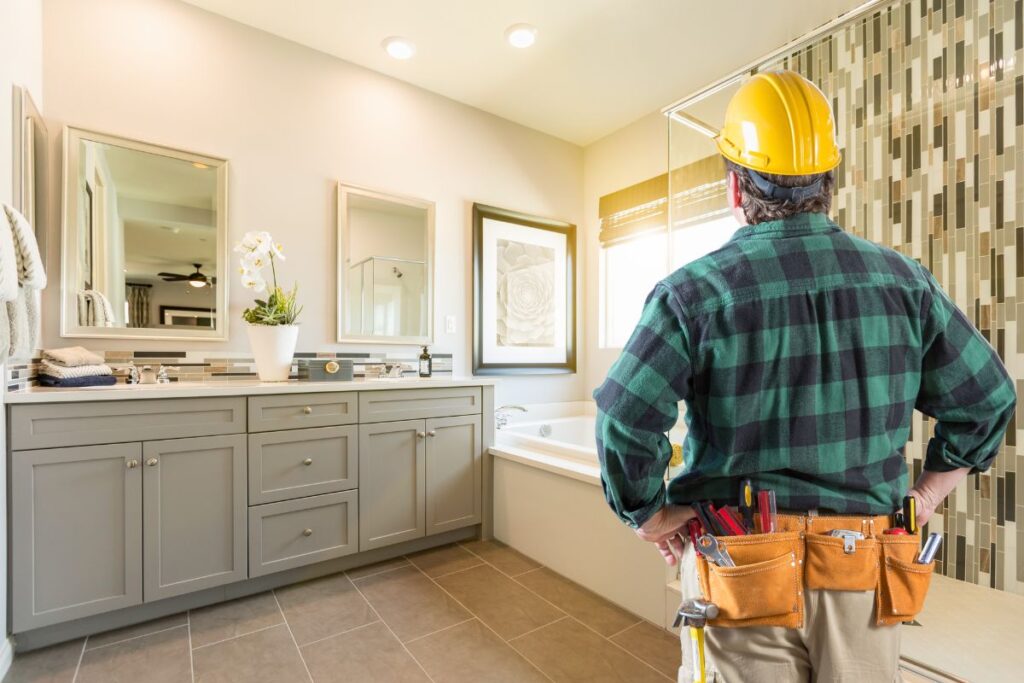 Image of a man in a green plaid shirt, wearing a hard hat, with his hands on his hips, looking at a kitchen he is going to hopefully win a bid to remodel. 